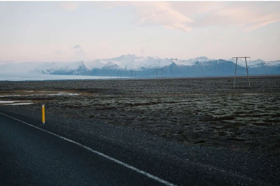 Asphalt road stretches into the distance toward mountains under a sky with scattered clouds during the daytime in an outdoor setting.
