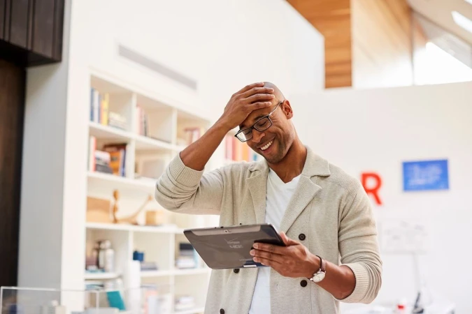Bald black man in glasses smiling and holding a tablet in a bright room