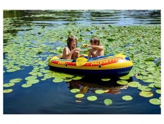 Two children sitting in a yellow and blue inflatable boat on a lake surrounded by lily pads