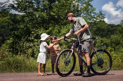 A man and two children by a bicycle on a dirt path, photographed by Claire And Jeremy Weiss.