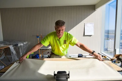 Middle-aged man wearing a lime green t-shirt unrolling wallpaper on a wooden table indoors.