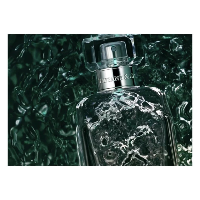 A close-up studio shot showcases a clear Tiffany & Co. perfume bottle against a textured dark green backdrop, emphasizing its luxurious design.
