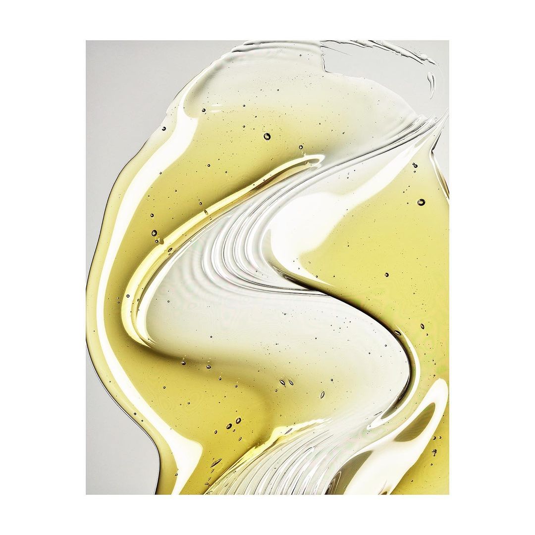 Close-up abstract beauty shot of clear and yellow cosmetic gel fluid with swirling lines and glossy textures on a light neutral surface.