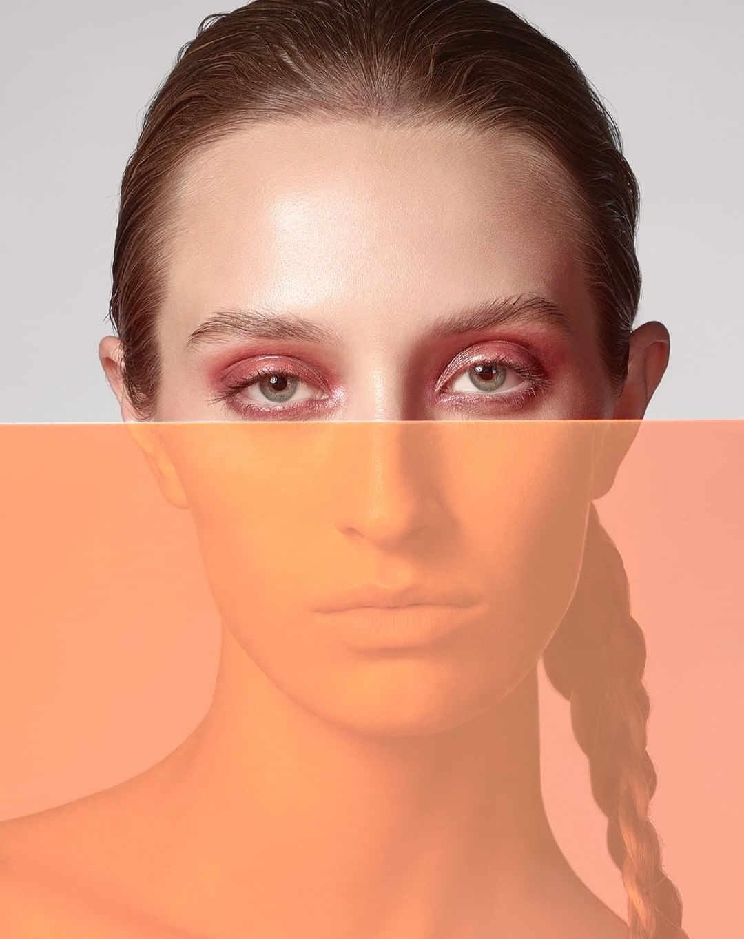 Close-up portrait of a woman with pink eyeshadow, orange gel filter on the lower part of her face, and a braided hairstyle.