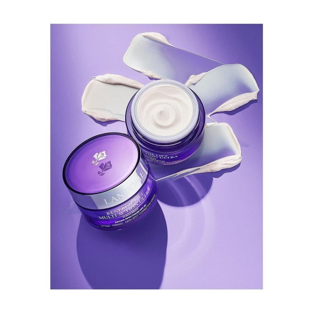 Two jars of Lancôme Rénergie Lift Multi-Action Ultra cream on a purple surface with smears of white cream in the background.
