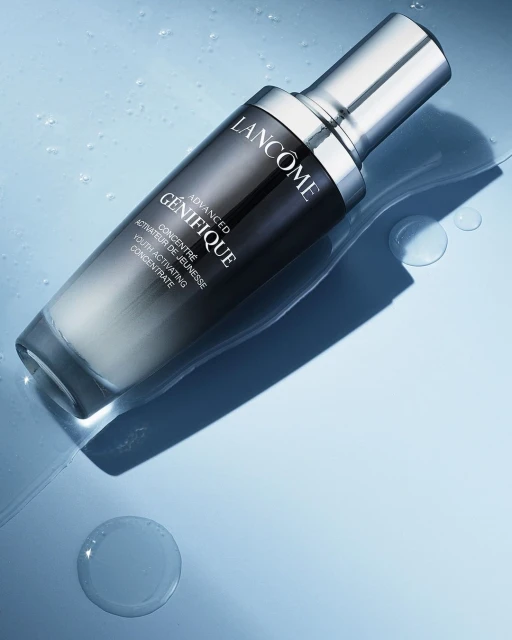Lancome Advanced Génifique youth activating concentrate bottle on a light blue surface with water droplets in a beauty product shot.