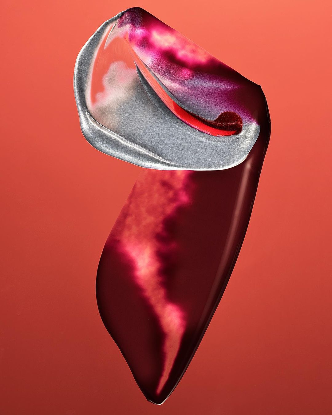 Abstract still life features a fluid, glossy material with a silver-gray edge against a red-orange background, showcasing depth and color transitions.