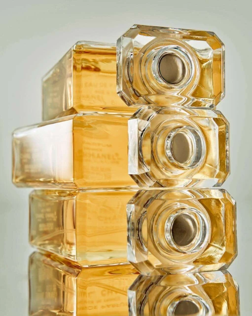 A stack of four crystal Chanel perfume bottles, featuring faceted geometric shapes and warm gold liquid, create a luxurious still life.