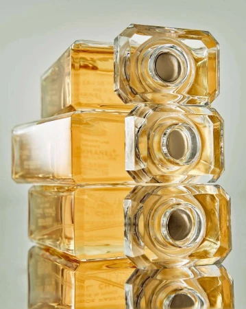 A stack of four crystal Chanel perfume bottles, featuring faceted geometric shapes and warm gold liquid, create a luxurious still life.