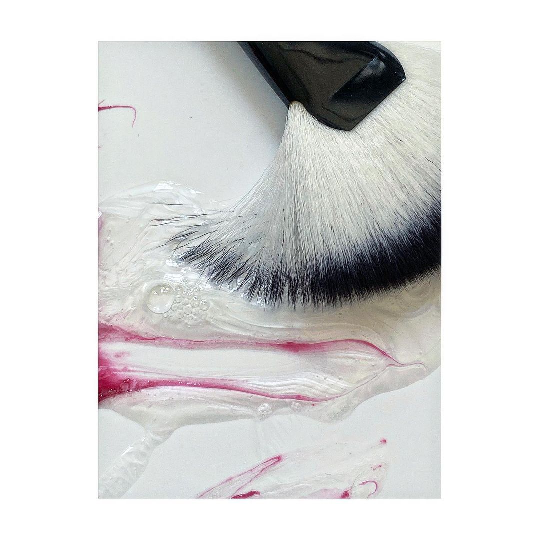 Close-up of a makeup brush with white bristles and a black handle sitting on top of a shimmery white and purple liquid base.