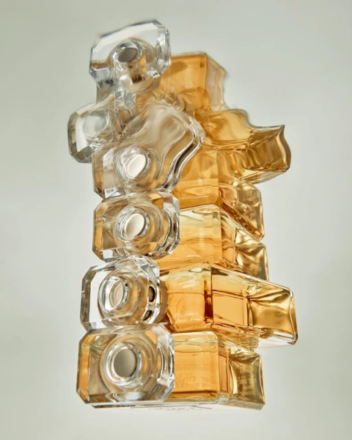 Abstract still life of stacked clear and amber glass perfume bottles, arranged vertically in a minimalist studio setting.