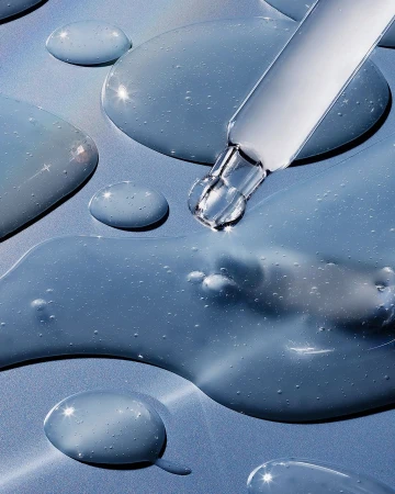 Close-up shot of clear beauty serum with a dropper on a light blue background, creating a clean and clinical aesthetic.