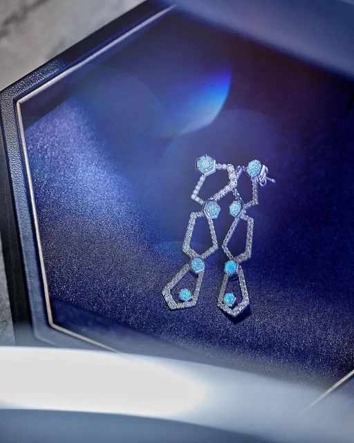 Elegant geometric earrings in a dark blue jewelry box with soft lighting enhancing the gems. Modern jewelry photography.