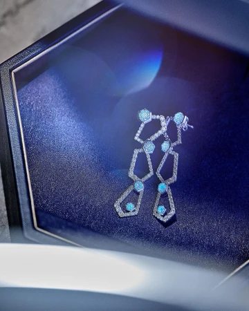 Elegant geometric earrings in a dark blue jewelry box with soft lighting enhancing the gems. Modern jewelry photography.