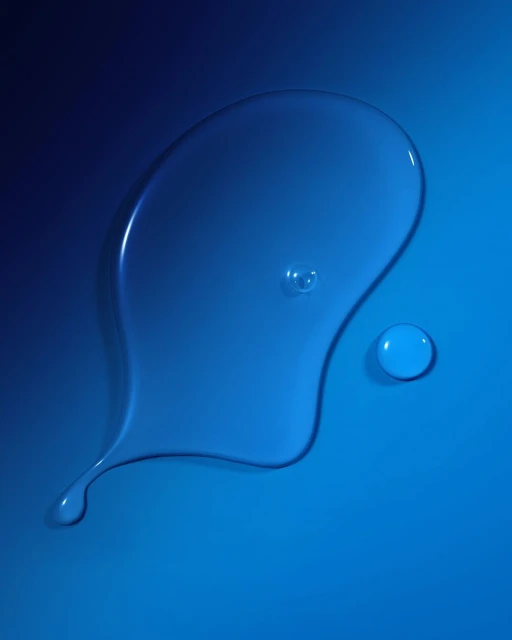 Close-up of a translucent liquid splash with small droplets scattered around against a gradient blue background. Cosmetic concept.