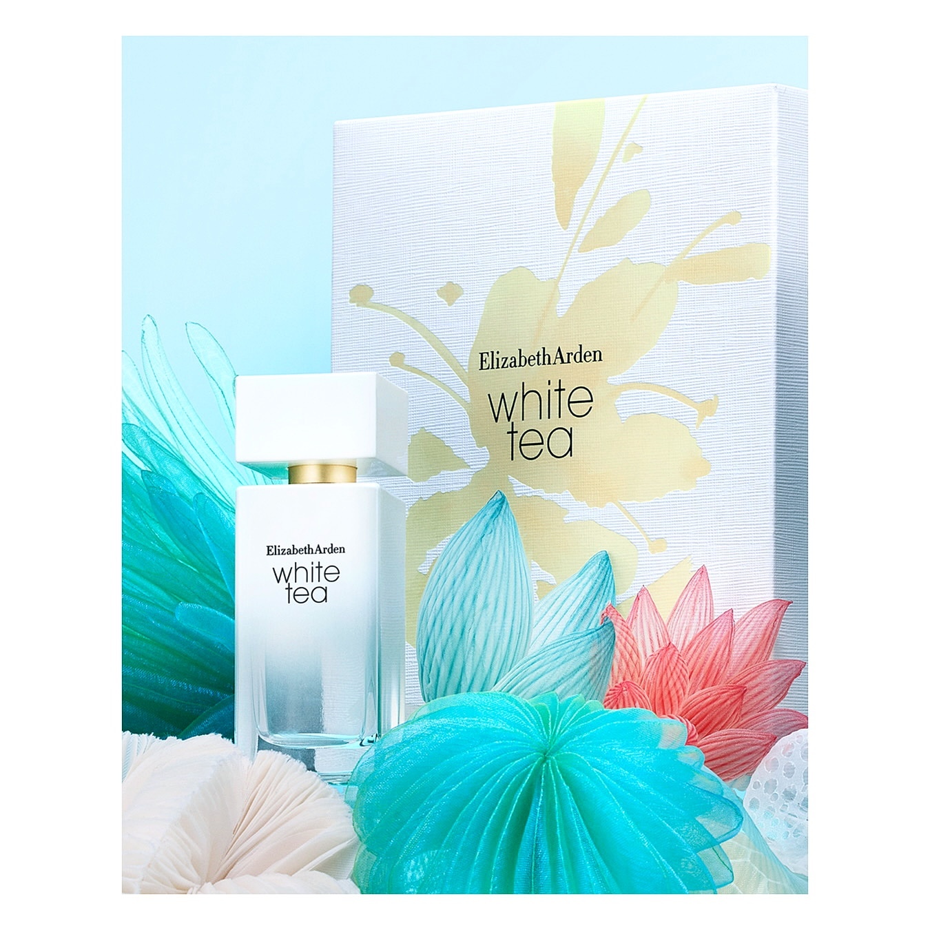 Elegant studio shot of Elizabeth Arden White Tea perfume with a decorative gift box and colorful paper flower accents on a light blue backdrop.