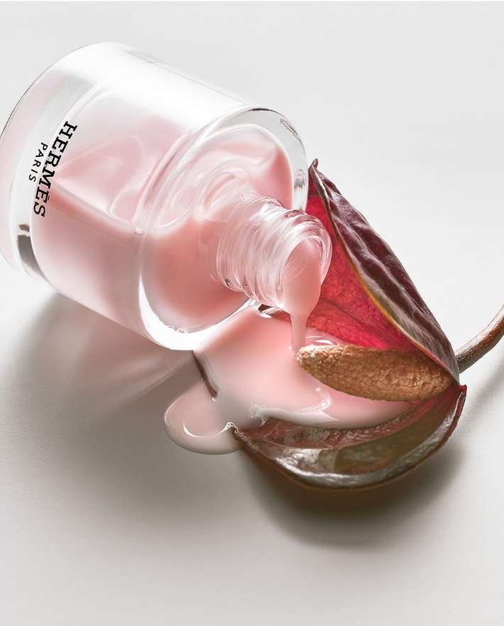 Pink nail polish bottle tipped with dripping polish onto purple leaf on a white surface, showcasing a beauty product close-up.