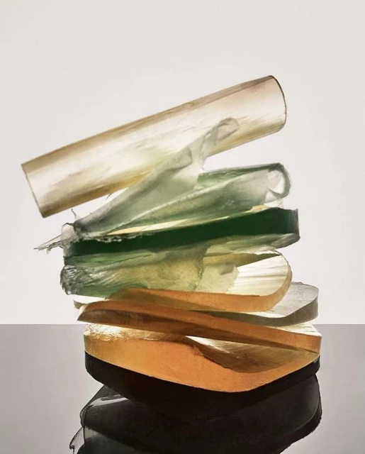 Stack of translucent sheets of material in shades of gold, green, and clear. The materials reflect a dark surface.
