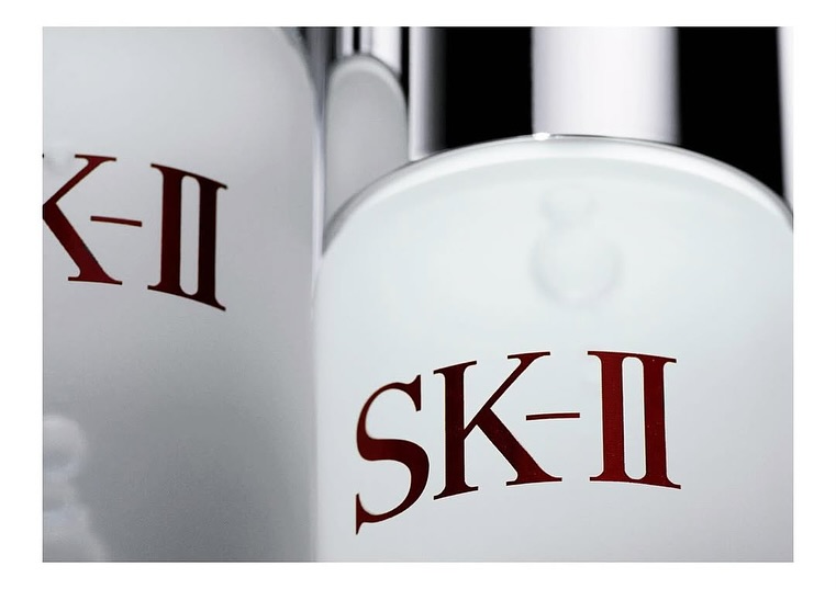Close-up product shot of SK-II skincare bottles. Red SK-II brand lettering on a white bottle with a silver cap against a dark background.