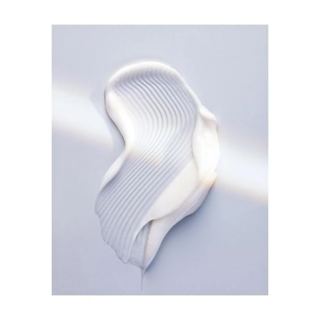 Close-up of a creamy white skincare product swatch with linear texture on a light blue surface, showcasing beauty product consistency.