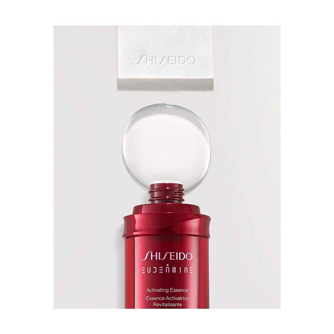 Still life of a red Shiseido Eudermine Revitalizing Essence bottle with a clear orb on top and a white cleansing cotton square.