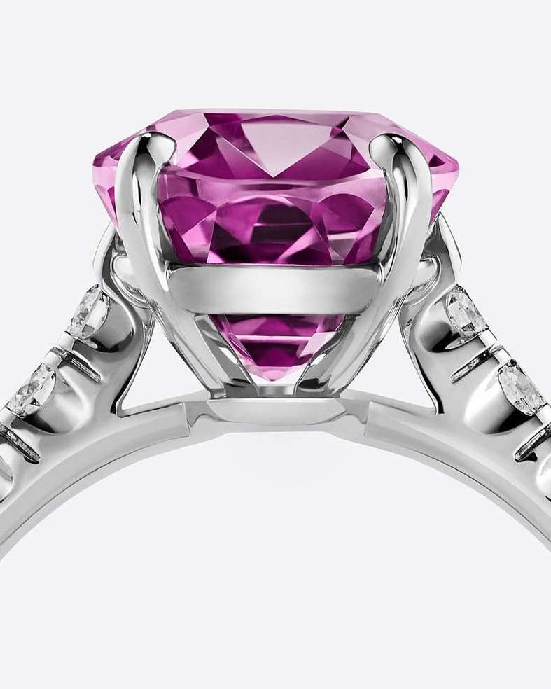 Close-up studio shot of a platinum ring with a large, round, faceted pink gemstone. Diamond accents sparkle on the ring's band.