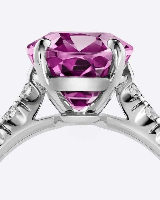 Close-up studio shot of a platinum ring with a large, round, faceted pink gemstone. Diamond accents sparkle on the ring's band.