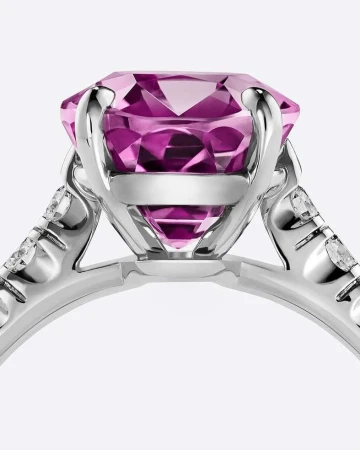 Close-up studio shot of a platinum ring with a large, round, faceted pink gemstone. Diamond accents sparkle on the ring's band.