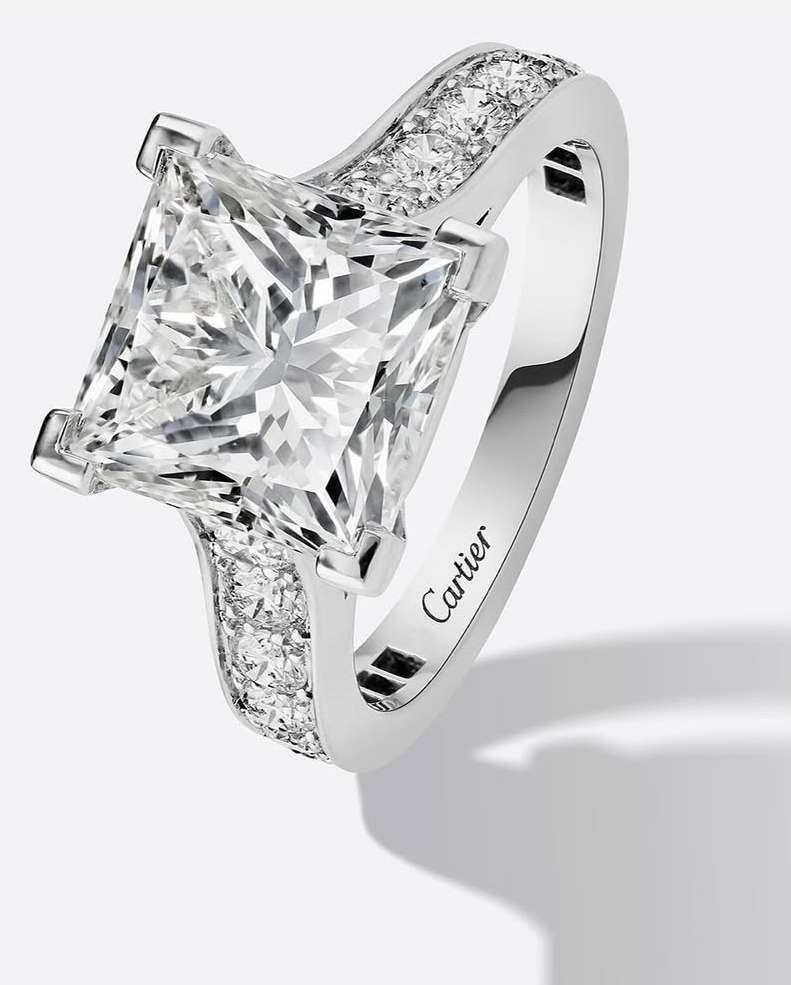 Close-up of a princess-cut diamond engagement ring with a platinum band and accent diamonds, set against a neutral backdrop.