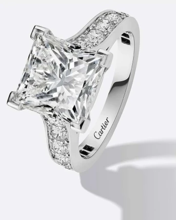 Close-up of a princess-cut diamond engagement ring with a platinum band and accent diamonds, set against a neutral backdrop.