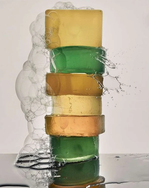 Stacked colorful bars of artisanal soap with bubbles and splashes, glossy surface, and a bright studio setting.