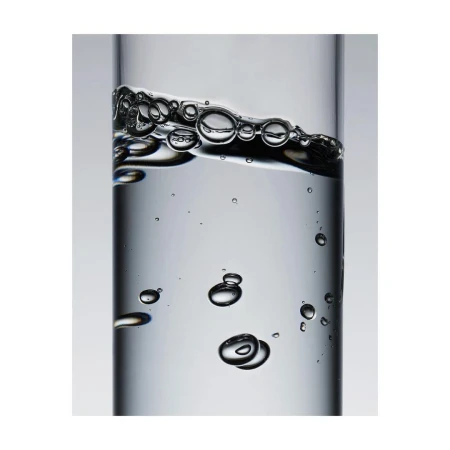A close-up photo of clear liquid and bubbles inside a transparent glass container on a light gray background, creating a minimalist still life.