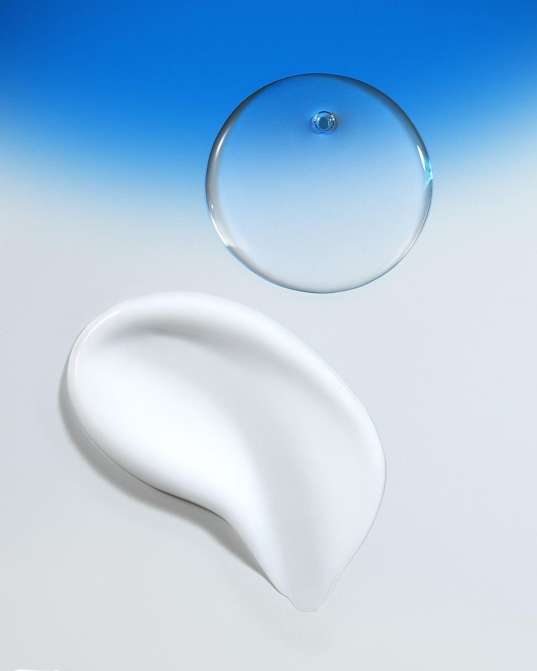Close-up shot of a smear of white cream and a clear serum bubble against a blue gradient background, evoking skincare and beauty.