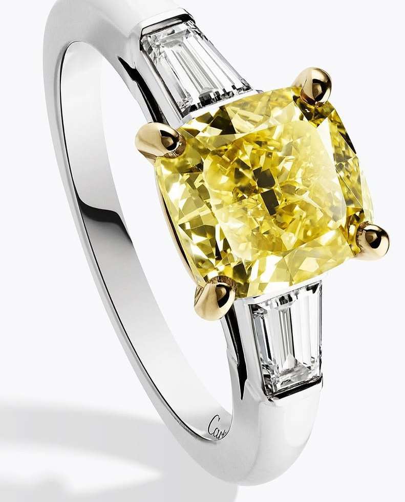 Close-up of a gemstone ring featuring a large cushion-cut yellow diamond flanked by baguette-cut diamonds set in a white gold band.