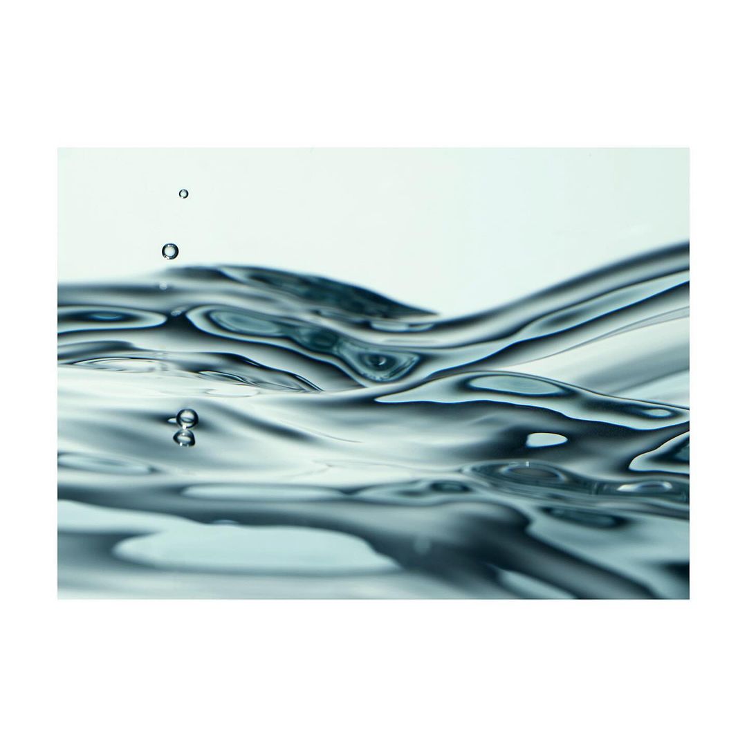 Clear water surface with ripples and small droplets against a light background, highlighting fluid dynamics and minimalist composition.