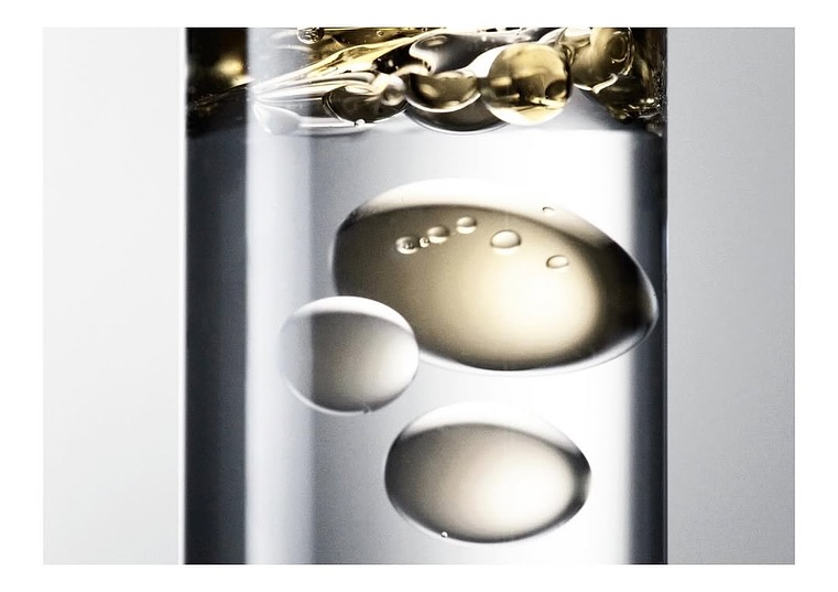 Close-up of clear glass cylinder with spheres of translucent liquid, creating abstract patterns in neutral color palette.