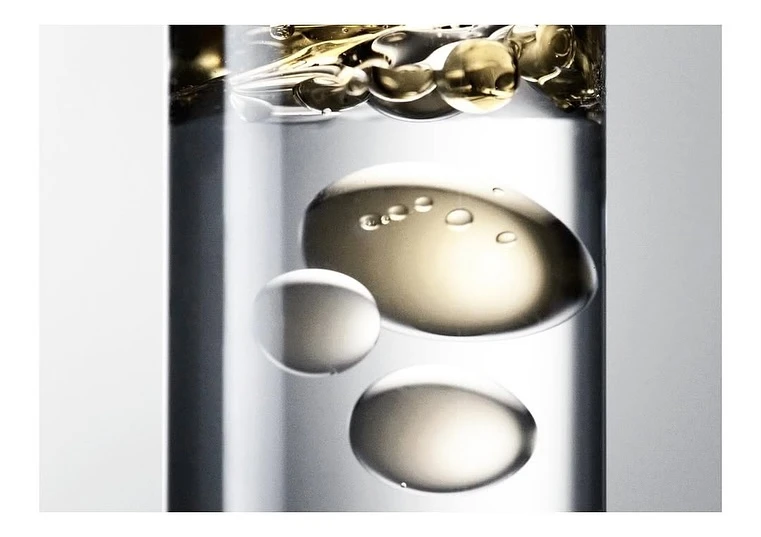 Close-up of clear glass cylinder with spheres of translucent liquid, creating abstract patterns in neutral color palette.