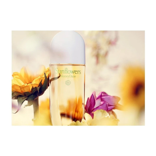 Close-up of a perfume bottle surrounded by yellow and pink flowers, with the brand 'Sunflowers' visible, set against a blurred background.