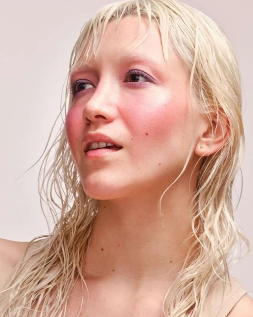 Portrait of a fair-skinned adult female with wet blonde hair, light pink makeup, and a neutral facial expression, against a neutral background.