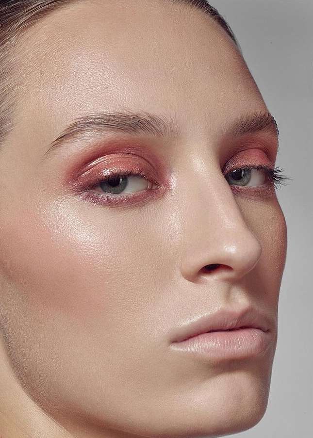 Close-up of a female model with pink eye makeup and glossy skin, showcasing beauty and cosmetics in a photo studio setting.