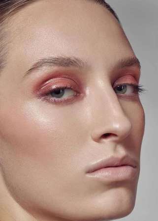 Close-up of a female model with pink eye makeup and glossy skin, showcasing beauty and cosmetics in a photo studio setting.