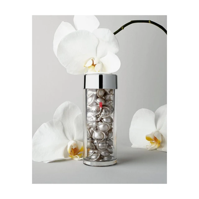 Clear container of Elizabeth Arden Advanced Ceramide capsules surrounded by white orchid blossoms on a light gray surface.
