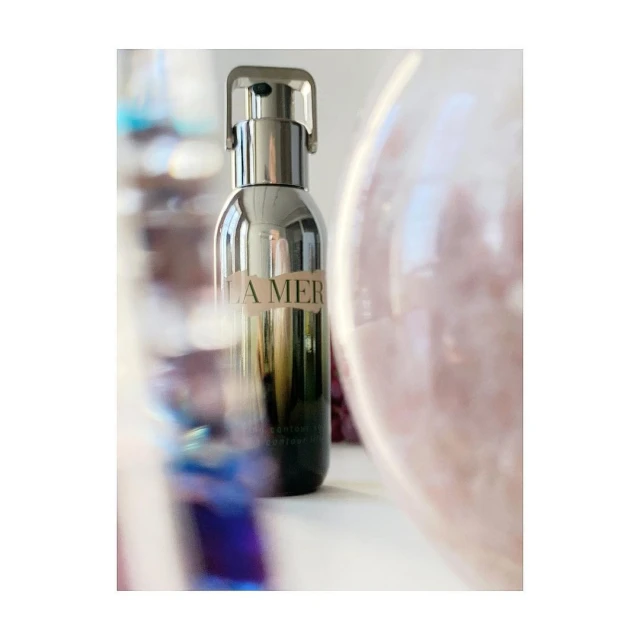 Close-up of a La Mer moisturizing renewal serum bottle with chrome pump, against a blurred background, creating a beauty product image.