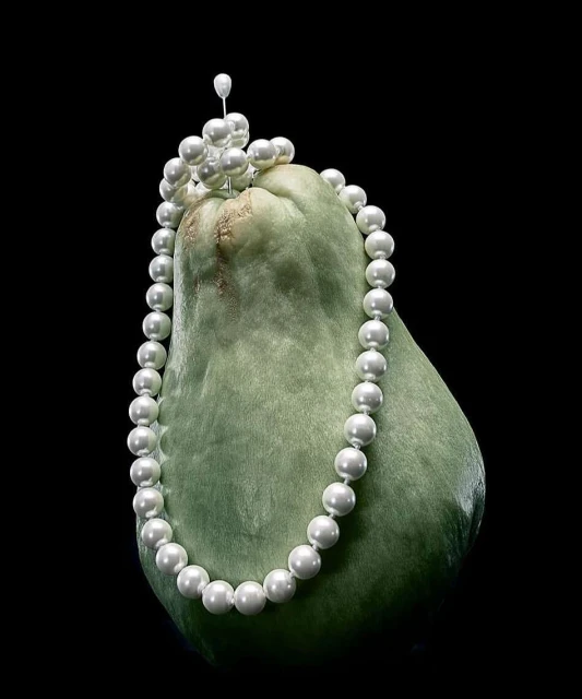 Chayote squash styled with a pearl necklace, creating a unique still life against a dark background, highlighting texture and color.