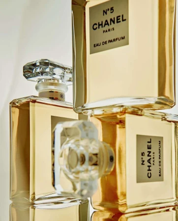 Three Chanel N°5 Eau de Parfum bottles stacked, clear crystal stoppers, gold liquid, white labels with black text, minimalist product photography.