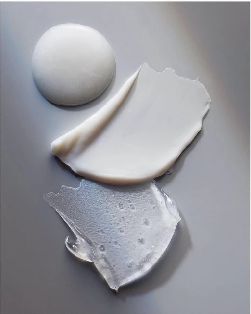 Close-up studio shot of a collection of skincare product textures, including a thick white cream, lotion smear, and clear gel, on gray.