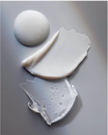 Close-up studio shot of a collection of skincare product textures, including a thick white cream, lotion smear, and clear gel, on gray.
