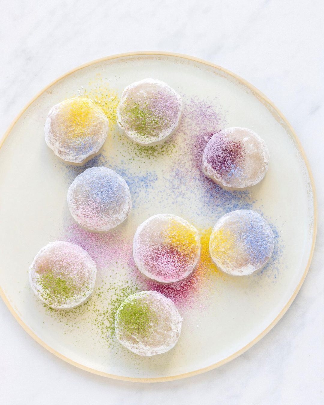 Overhead shot of colorful mochi balls on a plate, dusted with colored powders. Food photography showing Japanese sweets on white surface.