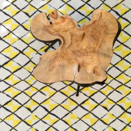 Live edge wood slice table resting on a patterned yellow and white rug with black crisscross lines.
