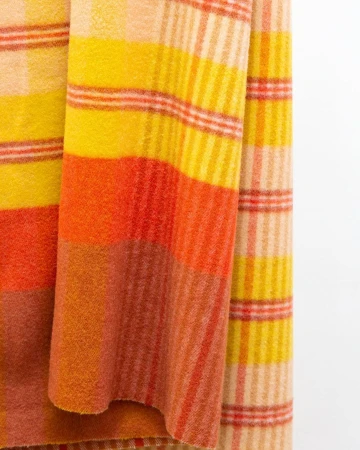 Close up of yellow and orange plaid wool blanket draped against a white wall.